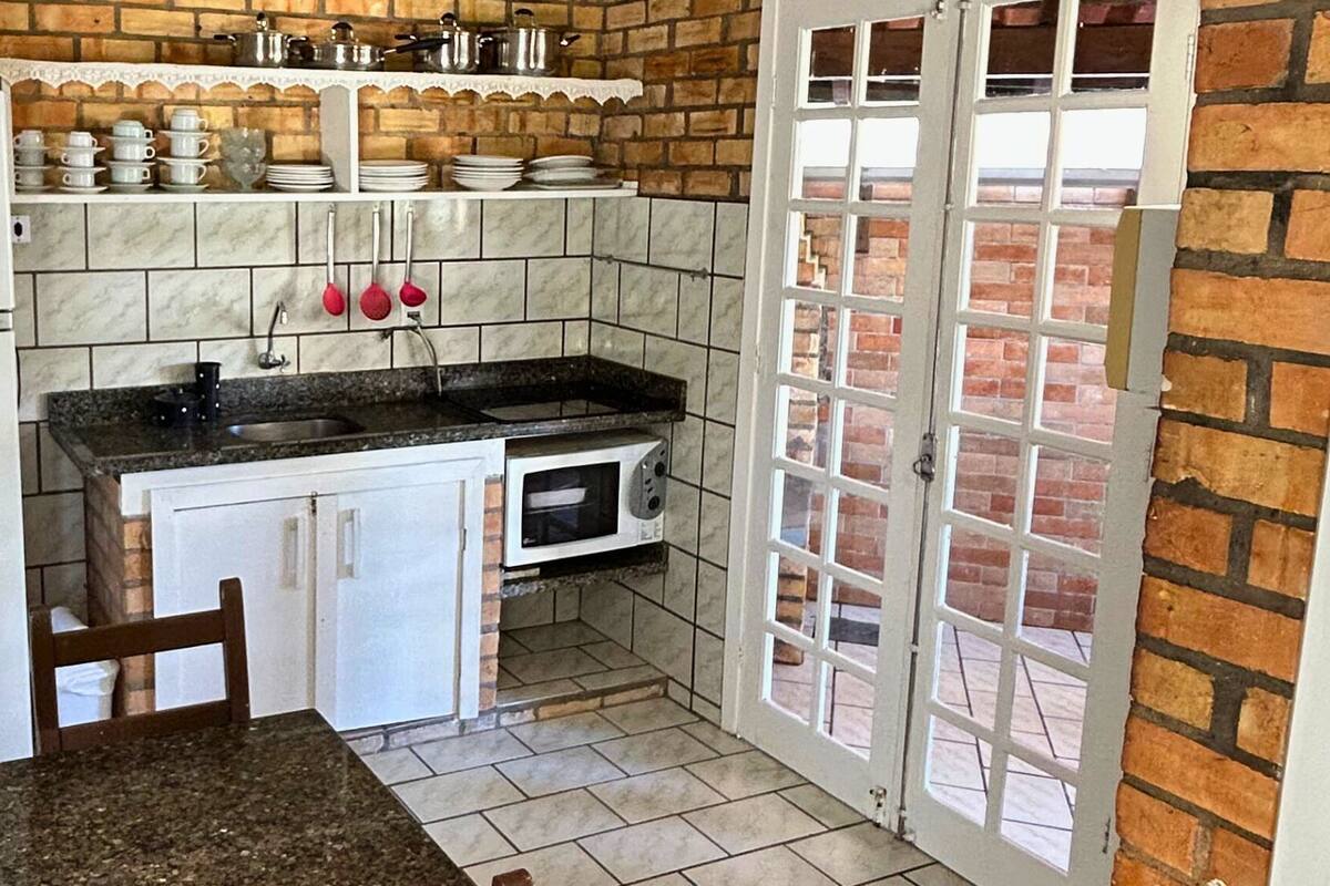 A compact kitchen with a refrigerator, sink, and cabinets. There is a window with a view of a brick wall and a door leading outside.