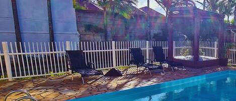 A swimming pool with a white fence, lounge chairs, and palm trees in the background.