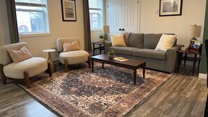 Ein Wohnzimmer mit einer Couch, zwei Sesseln, einem Couchtisch, einem Teppich und zwei Nachttischen mit Lampen.