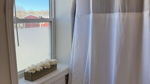 Ein Badezimmer mit Fenster, einer Duschvorhang und einem kleinen Tisch.