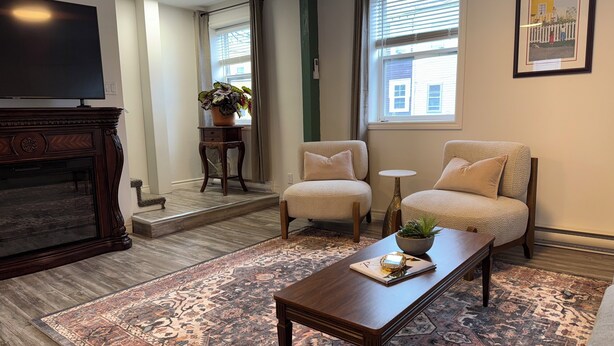 Ein Wohnzimmer mit Kamin, zwei Sesseln, einem Couchtisch, einem Teppich und einem Fernseher.