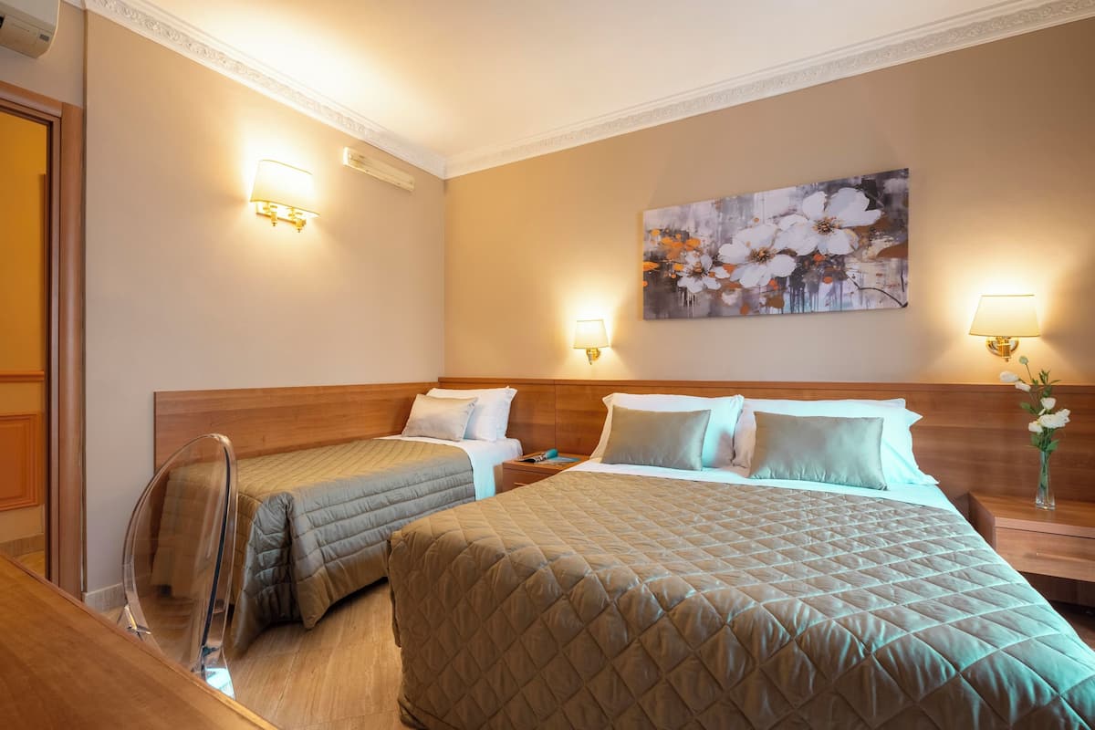 Hotellihuone, jossa on kaksi sänkyä, puinen pääty, seinällä oleva kukka-aiheinen taulu ja kaksi seinään kiinnitettyä lamppua.