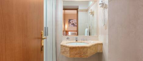 A bathroom with a marble sink, a glass shower enclosure, and a telephone mounted on the wall.
