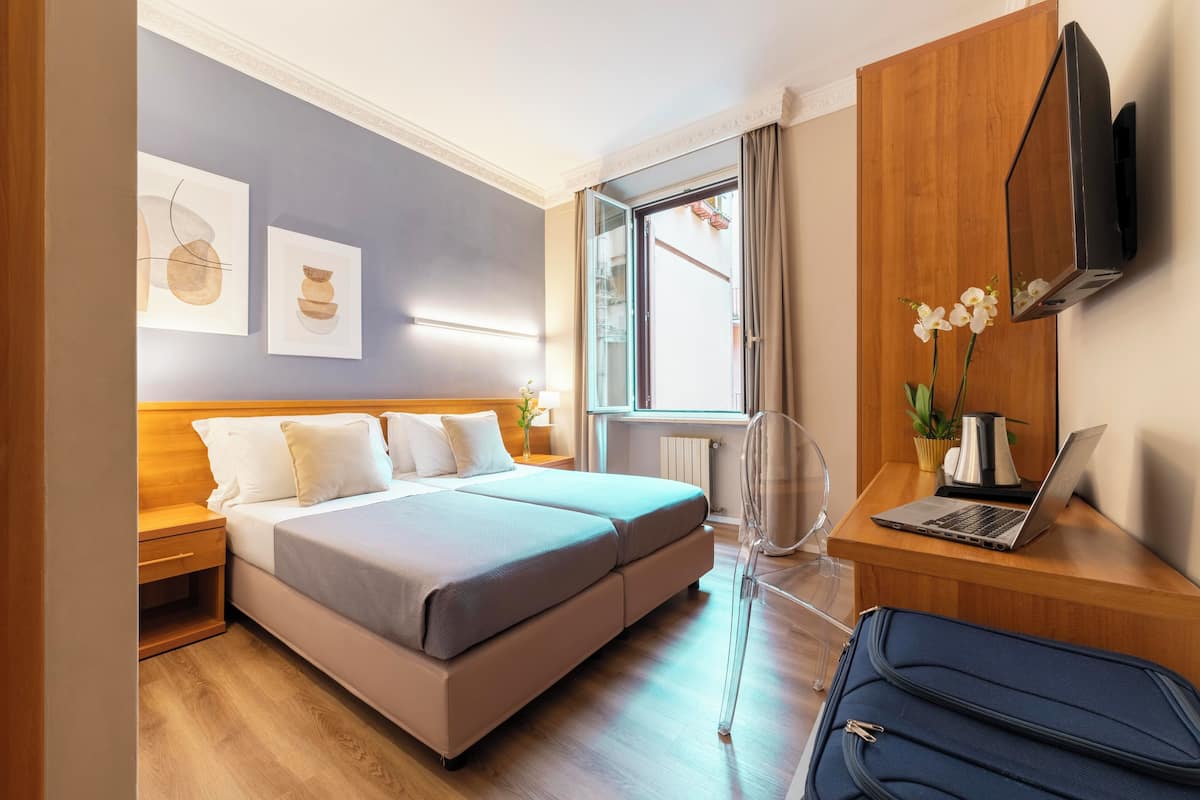 Moderni hotellihuone, jossa on sänky, työpöytä kannettavalla tietokoneella, televisio ja taideteoksia seinällä.