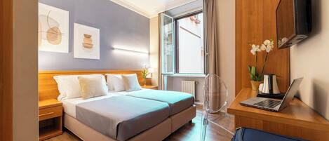 A modern hotel room with a bed, a desk with a laptop, a TV, and artwork on the wall.