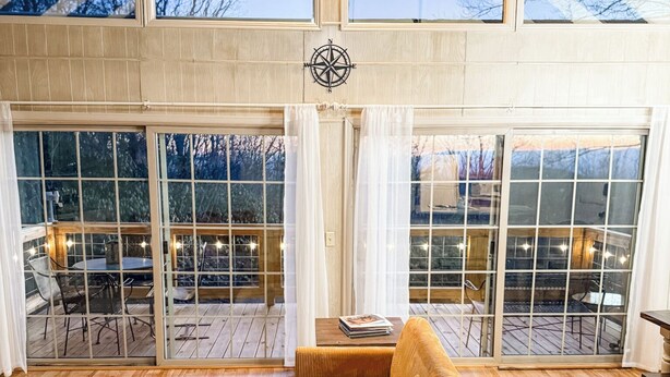 A spacious living area with a large window overlooking a deck, a wooden sofa, and a small table with a basket. - "18 Seasons" Seconds to Blue Ridge Parkway, & Mabry Mill. Game room w/Bar (Hillsville)