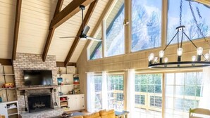 A spacious living area with a fireplace, wooden beams, large windows, and a dining table. - "18 Seasons" Seconds to Blue Ridge Parkway, & Mabry Mill. Game room w/Bar (Hillsville)