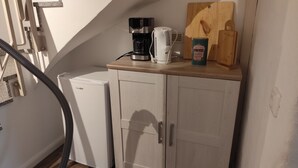 Une cuisine compacte équipée d’une machine à café, d’une bouilloire et d’une planche à découper sur le plan de travail.