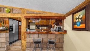 A kitchen with a wooden bar, two bar stools, a refrigerator, and a painting on the wall. - Family Chalet in Villa Vicente 4 BR (Villa Guerrero)