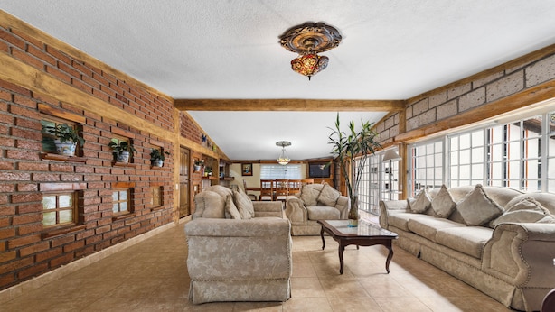 A spacious living room with a brick wall, a large sofa, a smaller armchair, and a coffee table. - Family Chalet in Villa Vicente 4 BR (Villa Guerrero)