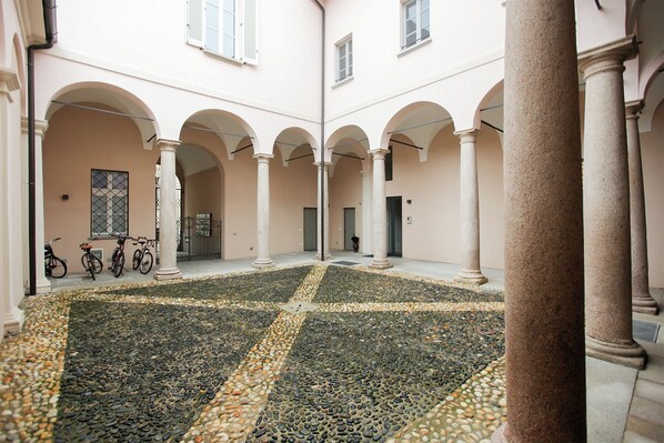 Un patio con piso de mosaico de guijarros, columnas y bicicletas estacionadas contra la pared.