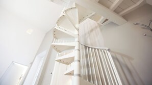 Un escalier en colimaçon avec des rampes et une main courante blanches, menant à l’étage supérieur.