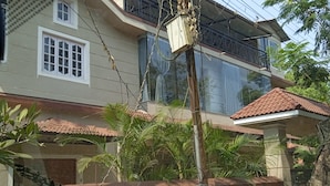 Een tweelaags huis met een balkon, een zichtbare elektriciteitskast en een dak van rode tegels.