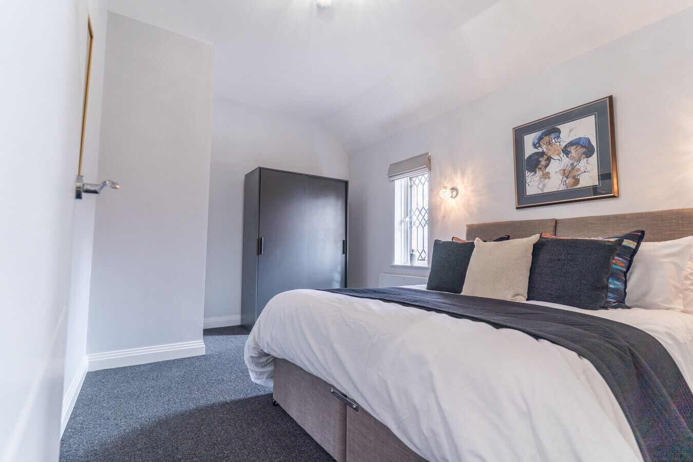 A bedroom with a bed, a wardrobe, a window with a view, and a painting on the wall.
