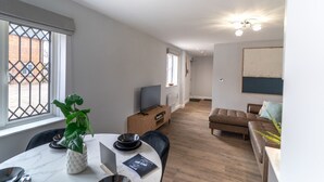 A modern living room with a TV, a brown leather sofa, and a dining area with a table set for two.
