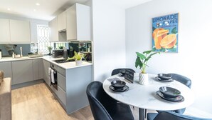 A modern kitchen with grey cabinets, a central island, and a dining area with a white table and black chairs.