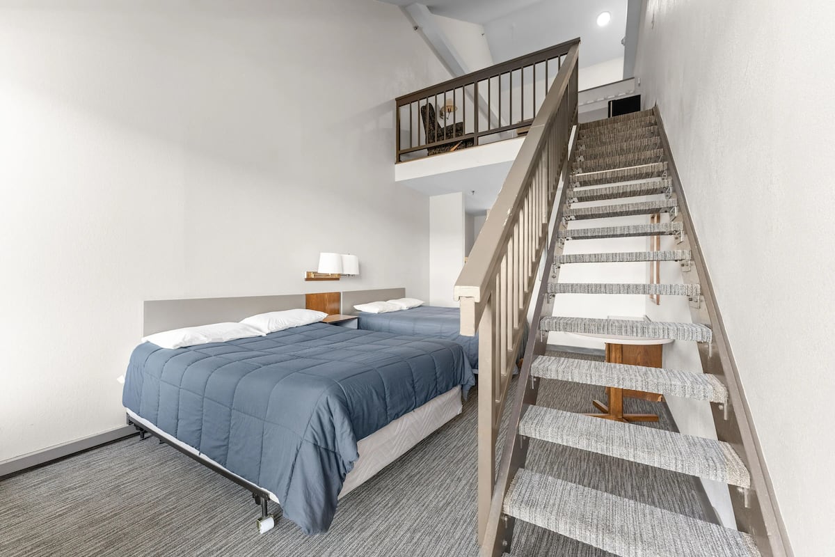 Een slaapkamer met een bed, een nachtkastje, een lamp en een trap.