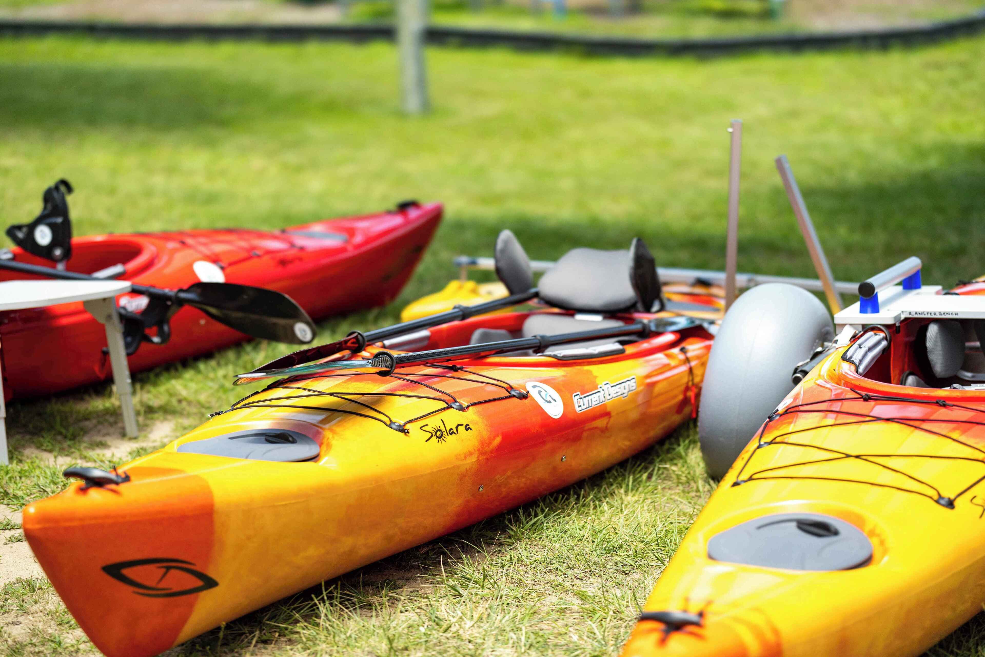 Three kayaks with paddles and a helmet on a grassy area.