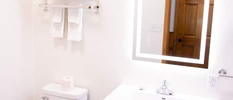 Un baño con inodoro, lavamanos con espejo y un perchero para toallas.