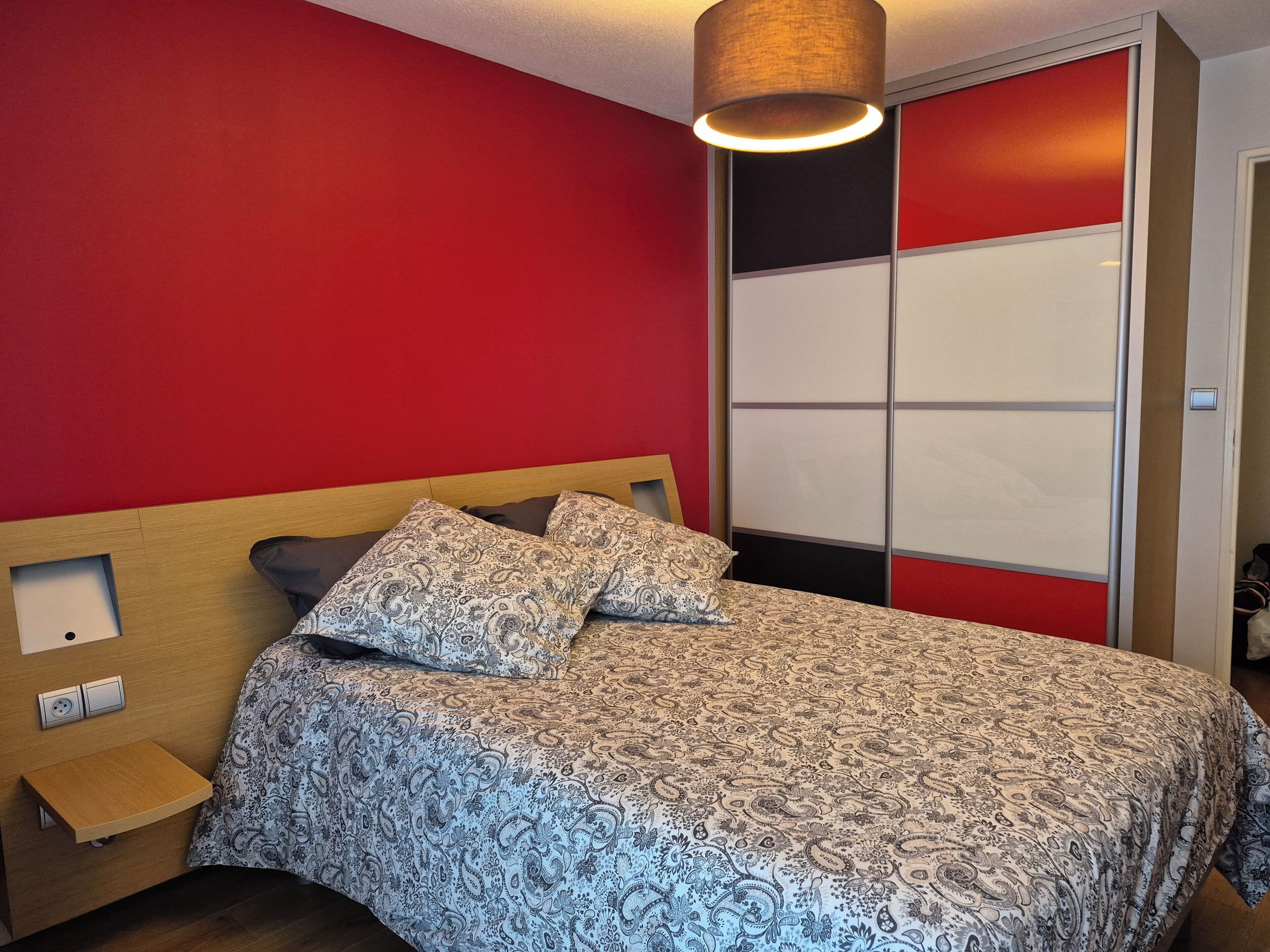 A bedroom with a bed, a nightstand, a wardrobe, and a hanging light fixture.