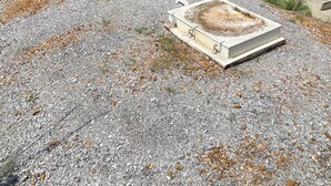 Ett område med grus, en planteringslåda i betong och två vita staketstolpar.