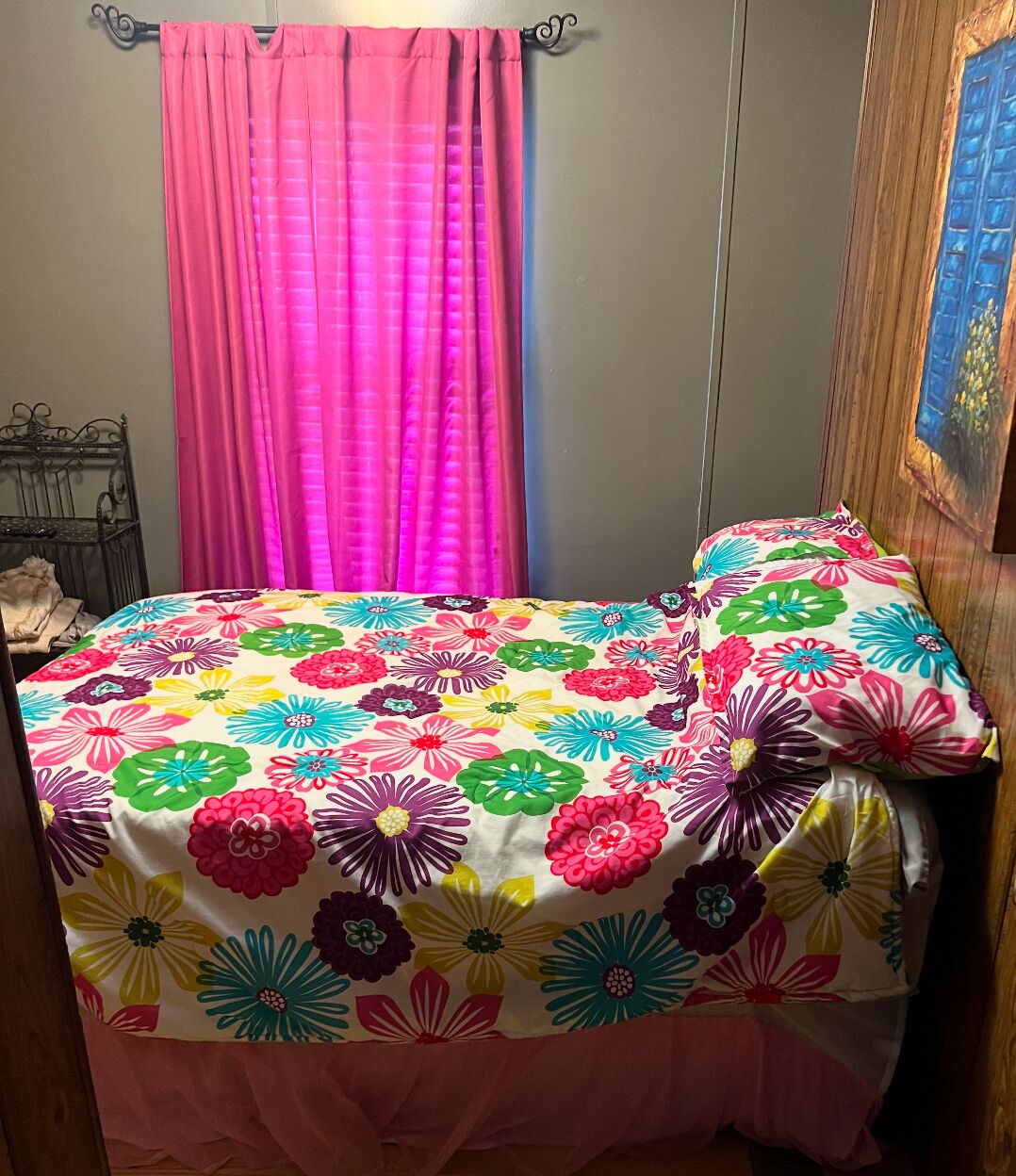 Une chambre à coucher avec une couvre-lit à motifs floraux colorés, des rideaux roses et une tête de lit en bois.