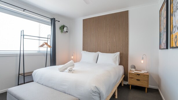 Una camera d'albergo moderna con un letto grande, un comodino, tende a una finestra e una pianta fissata alla parete.