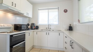 Una cucina moderna con mobili bianchi, un fornello, un forno a microonde, una macchina del caffè e un lavello.