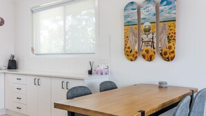 Una cucina moderna con una finestra, mobili bianchi, un tavolo da pranzo in legno e un'opera d'arte a parete raffigurante astronauti e girasoli.