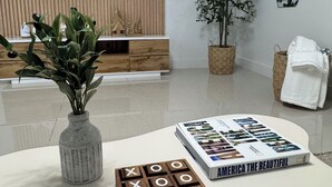 A modern living room with a flat-screen TV, wooden entertainment unit, a potted plant, a book titled "America the Beautiful", and a wooden board game. - Charming 1-bedroom apartment in North Bay Village with WiFi, AC (North Bay Village)