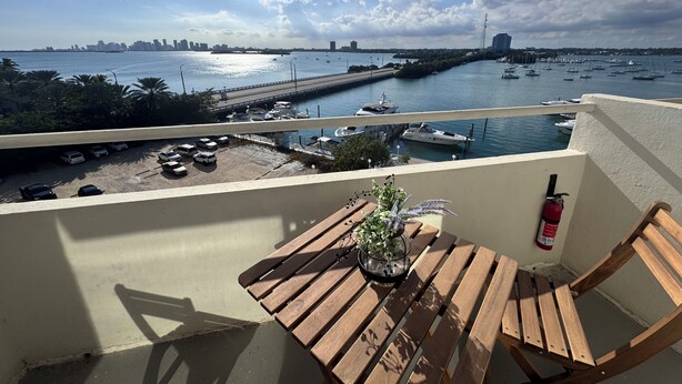 A balcony with a wooden table and chairs, overlooking a marina with boats and a city skyline. - Charming 1-bedroom apartment in North Bay Village with WiFi, AC (North Bay Village)
