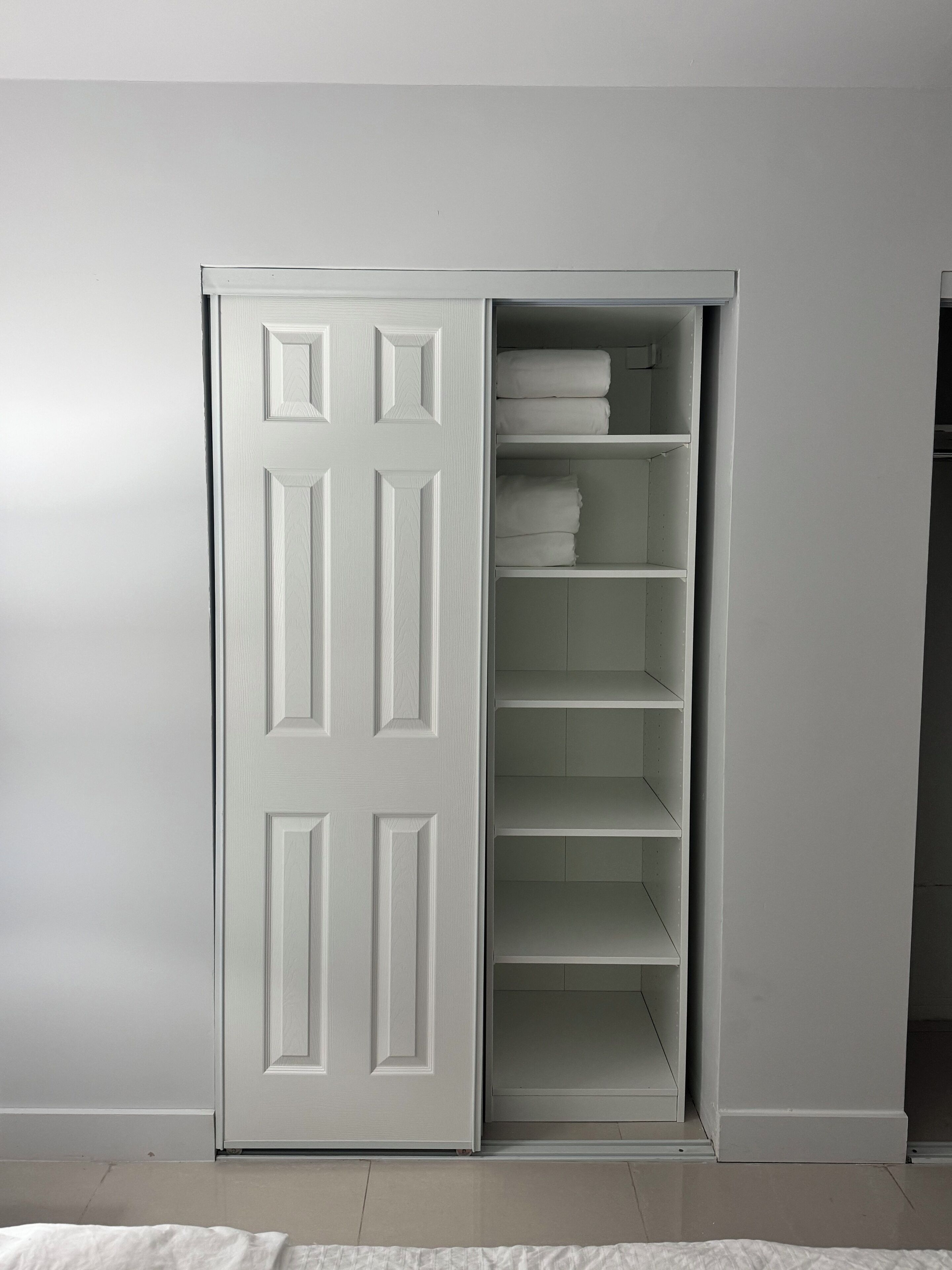 A white closet with multiple shelves and hanging space, featuring a sliding door.