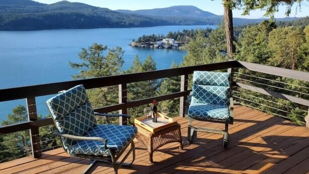 A wooden deck with two rocking chairs and a small table, overlooking a lake and forested hills. - Waterfront View Rosario Sleeps 10- (Eastsound)