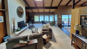 A spacious living room with a fireplace, comfortable seating, and large windows offering a view of the outdoors. - Waterfront View Rosario Sleeps 10- (Eastsound)