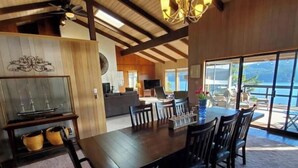 A spacious dining area with a long table and chairs, a television, and a view of the ocean through large windows. - Waterfront View Rosario Sleeps 10- (Eastsound)