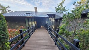 A wooden pathway leading to a modern building with a metal roof and a circular emblem on the facade. - Waterfront View Rosario Sleeps 10- (Eastsound)