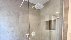 A modern shower with a glass door, a handheld showerhead, and a wall-mounted control panel.