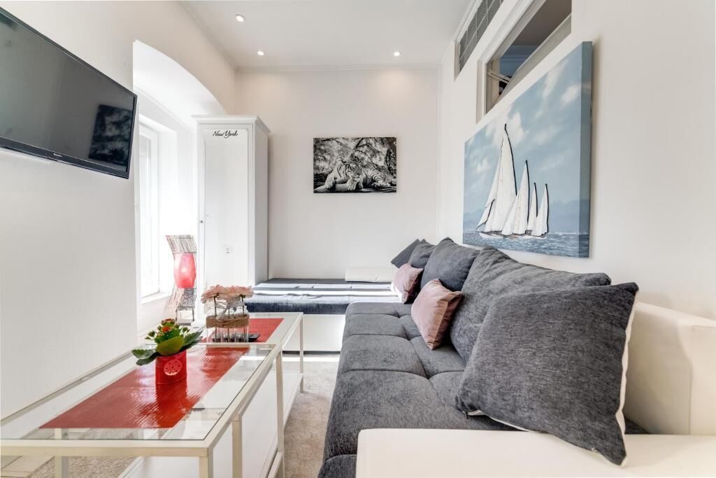 Een moderne woonkamer met een grijze bank, een rode tafel en kunstwerken aan de wanden.