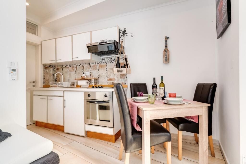 Cocina compacta con gabinetes blancos, un microondas y un horno pequeño. Una mesa de comedor con sillas está dispuesta en el centro.