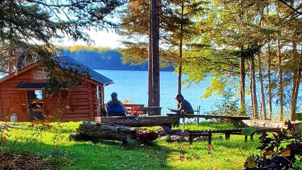 Une cabane avec un quai qui s’avance sur un lac, entourée d’arbres et d’herbe.