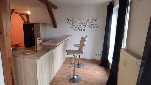 Une cuisine compacte dotée d’un plan de travail en bois, de deux tabourets de bar et d’un mur orné d’un motif décoratif.
