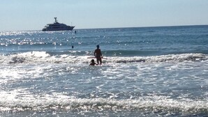 Una playa con olas, un barco a lo lejos y gente en el agua.