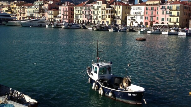 Un puerto con barcos amarrados, una torre destacada y edificios coloridos a lo largo del paseo marítimo.