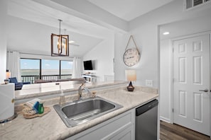 A modern kitchen with a sink, a dishwasher, and a large window overlooking a balcony.