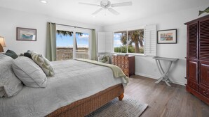 Ein Schlafzimmer mit einem großen Bett, einem Deckenventilator, einer hölzernen Kommode und Blick auf den Strand.