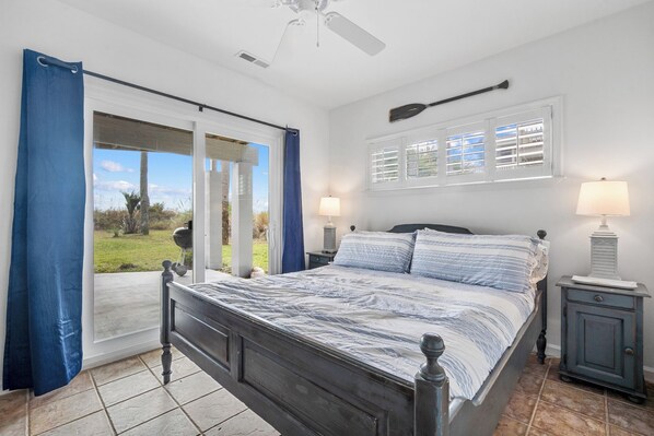 A bedroom with a bed, two bedside tables, a ceiling fan, a window with shutters, and a view of the outdoors. - Beachfront Home, Oceanfront, Dog Friendly - 710 Silverside (Fripp Island)