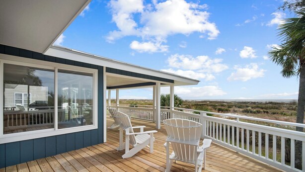 Eine Holzterrasse mit weißen Stühlen und Blick auf den Strand.