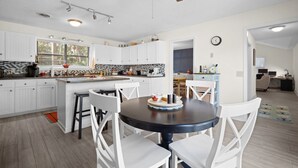 A modern kitchen with white cabinetry, a central island, and a dining area with white chairs. - Pet Friendly, Golf Course 3BR/3BA Home, 549 Remora Drive (Fripp Island)