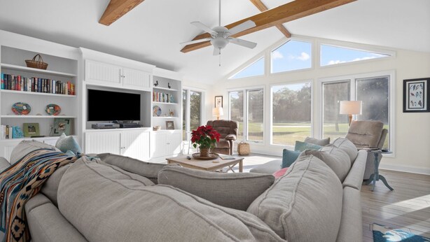 A spacious living room with a large sectional sofa, a flat-screen TV, and a ceiling fan. There are bookshelves and a dining area visible. - Pet Friendly, Golf Course 3BR/3BA Home, 549 Remora Drive (Fripp Island)