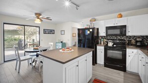 A modern kitchen with white cabinets, a black refrigerator, a microwave, and a stove. There is a dining area with a table and chairs, and a ceiling fan. - Pet Friendly, Golf Course 3BR/3BA Home, 549 Remora Drive (Fripp Island)